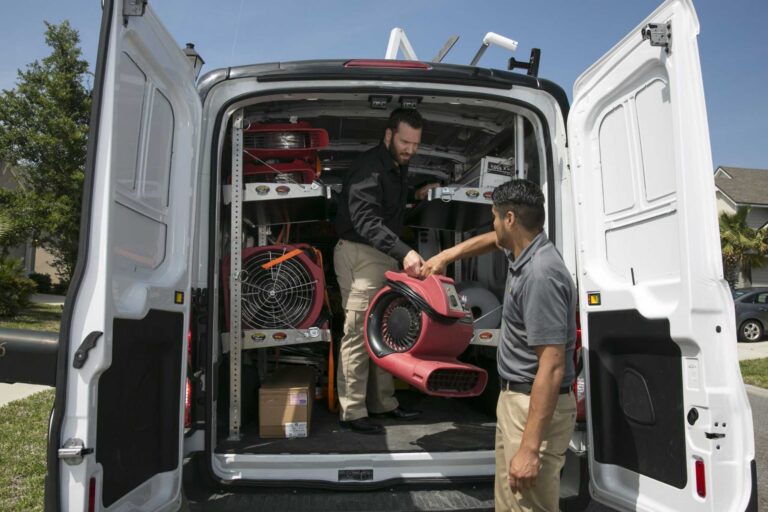 Paul Davis Restoration technicians unloading commercial air movers and drying equipment from service van for emergency water damage restoration in Central DFW.